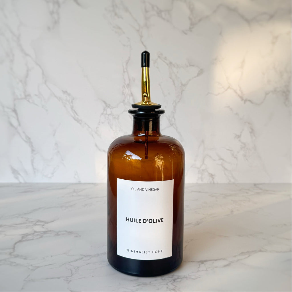 Duo de bouteilles en verre ambré avec bec verseur doré et noir, posées sur un plateau en bois, ambiance cuisine minimaliste et fonctionnelle.