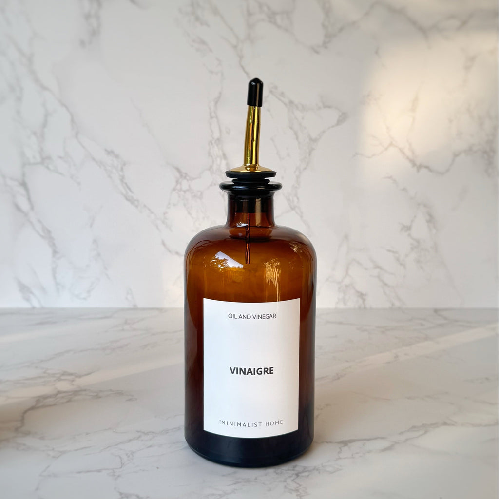 Duo de bouteilles en verre ambré avec bec verseur doré et noir, posées sur un plateau en bois, ambiance cuisine minimaliste et fonctionnelle.