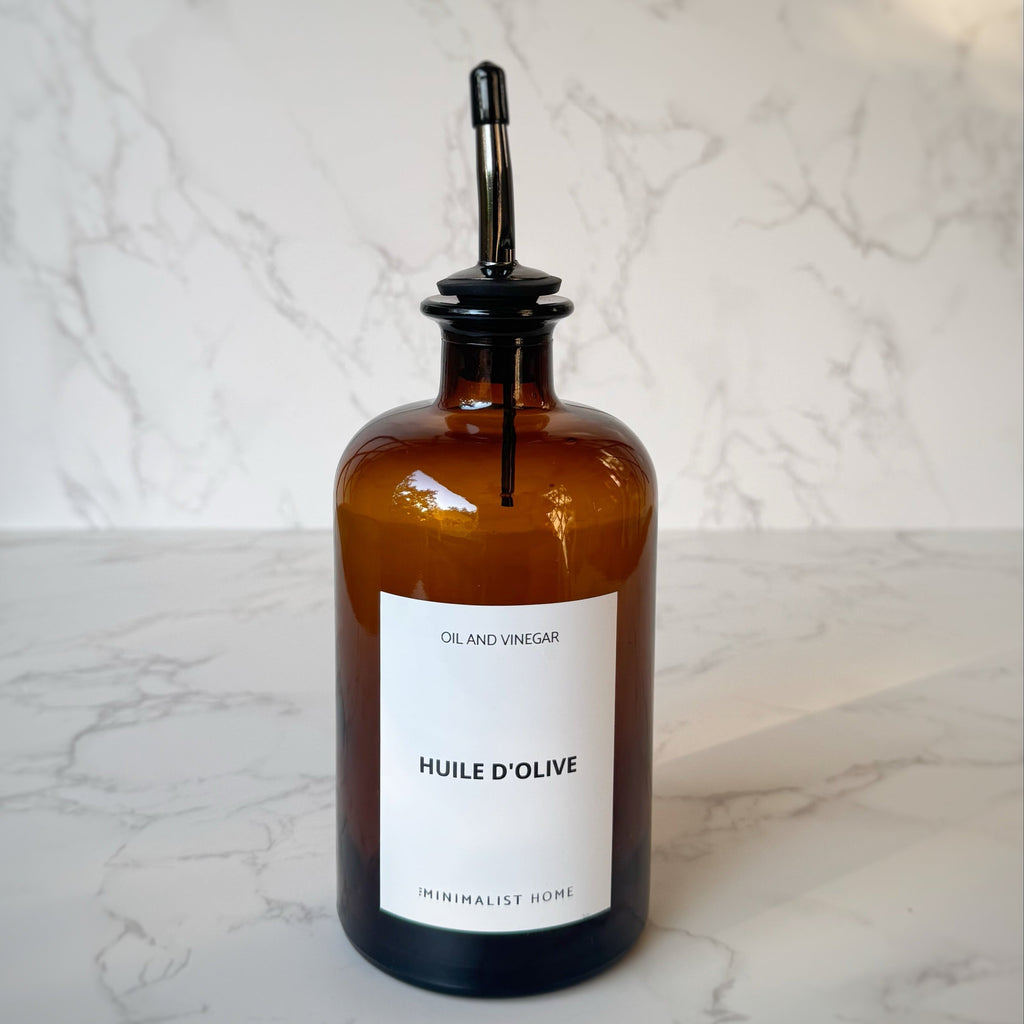 Duo de bouteilles en verre ambré avec bec verseur doré et noir, posées sur un plateau en bois, ambiance cuisine minimaliste et fonctionnelle.