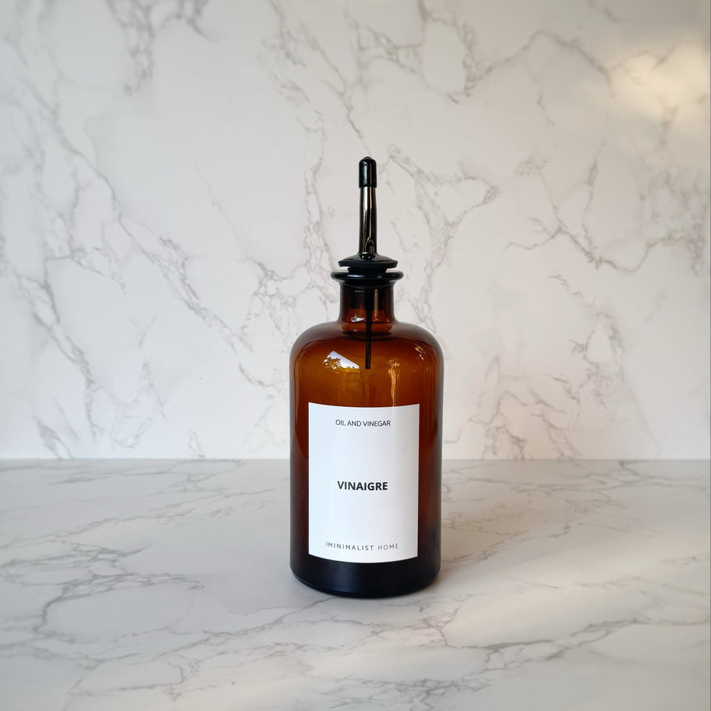Duo de bouteilles en verre ambré avec bec verseur doré et noir, posées sur un plateau en bois, ambiance cuisine minimaliste et fonctionnelle.